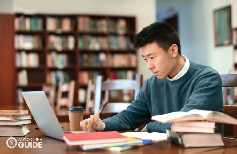 estudiante de doctorado estudiando en la biblioteca con su computadora portátil y libros