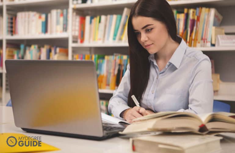 mujer estudiando con libros y una computadora portátil