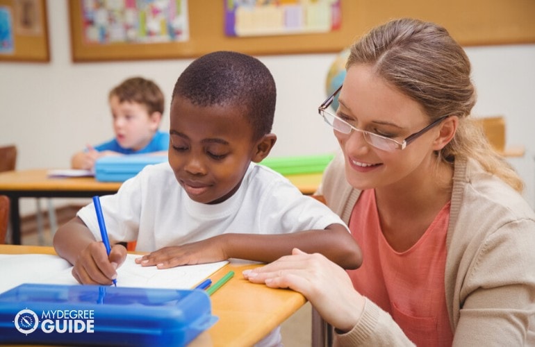 maestra de preescolar ayudando a su estudiante a escribir